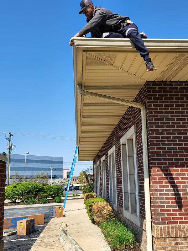 Installer hanging gutters along a commercial roofline