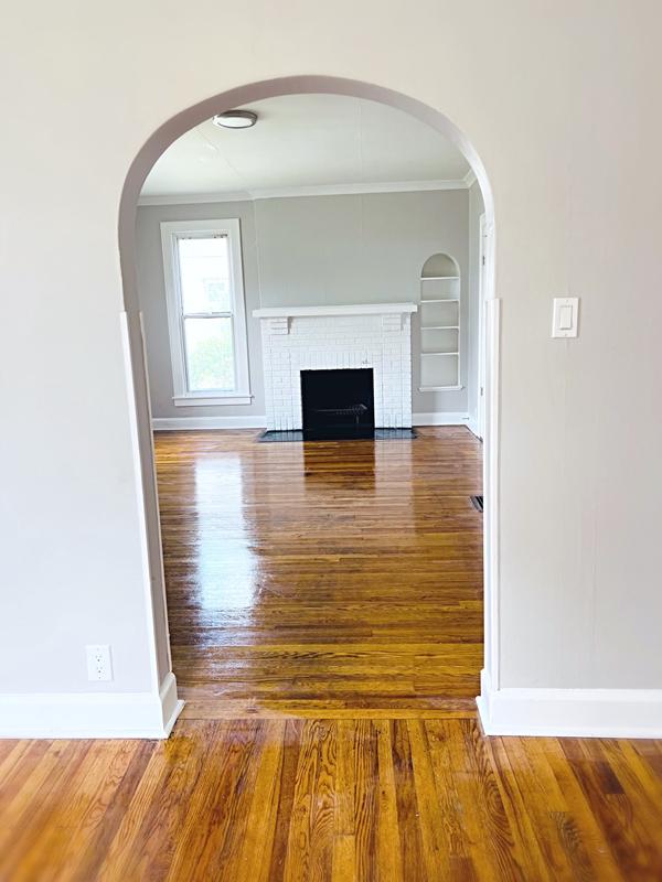 Refinished hardwood floors through an arched doorway to a fireplace